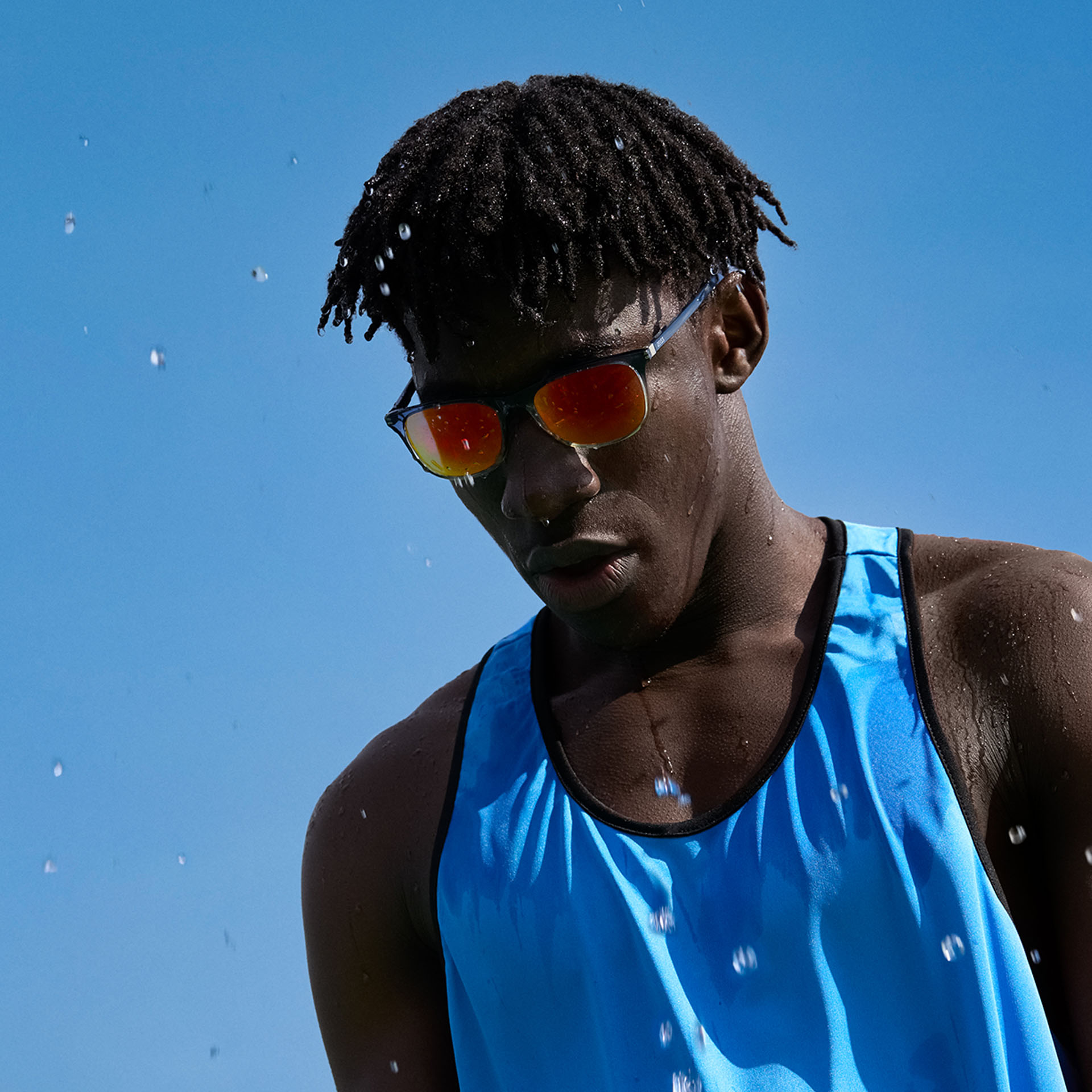 En ung mand i sportstøj og ZEISS Performance-solbrilleglas i en brun-orange tone foran den blå himmel.