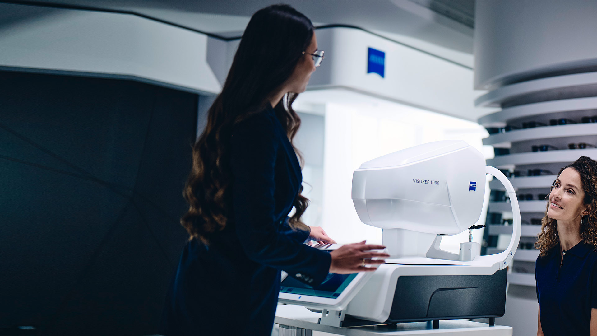 En kvinde sidder foran ZEISS VISUREF 1000 og ser på en kvindelig optiker.