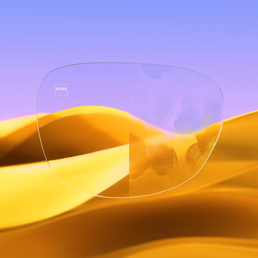 Et delt brilleglas med den ene side klar og ren med ZEISS DuraVision Gold UV og den anden side med fingeraftryk på glasset.