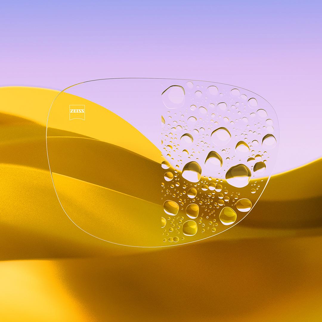 Et delt brilleglas med den ene side klar og ren med ZEISS DuraVision Gold UV og den anden side med vanddråber på glasset.