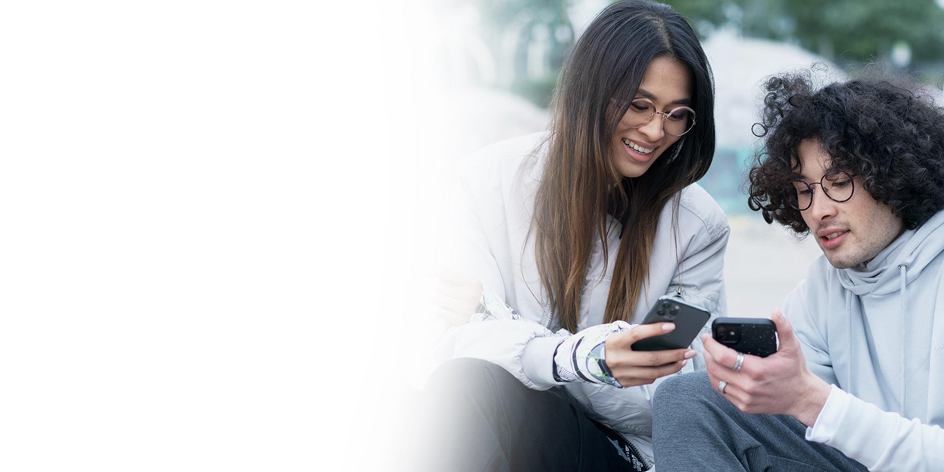 To unge mennesker, en kvinde med langt brunt hår, der smiler, og en dreng med krøllet sort hår, der bærer briller med ZEISS SmartLife-glas, og som alle kigger på deres telefoner. 