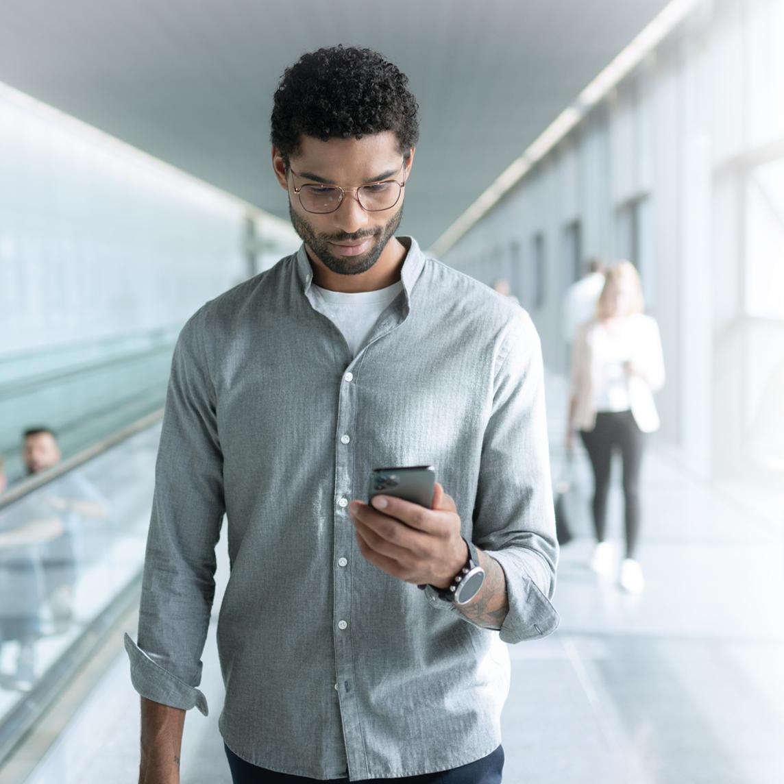 Ung mand med briller med ZEISS SmartLife-glas ser på sin telefon mens han går.