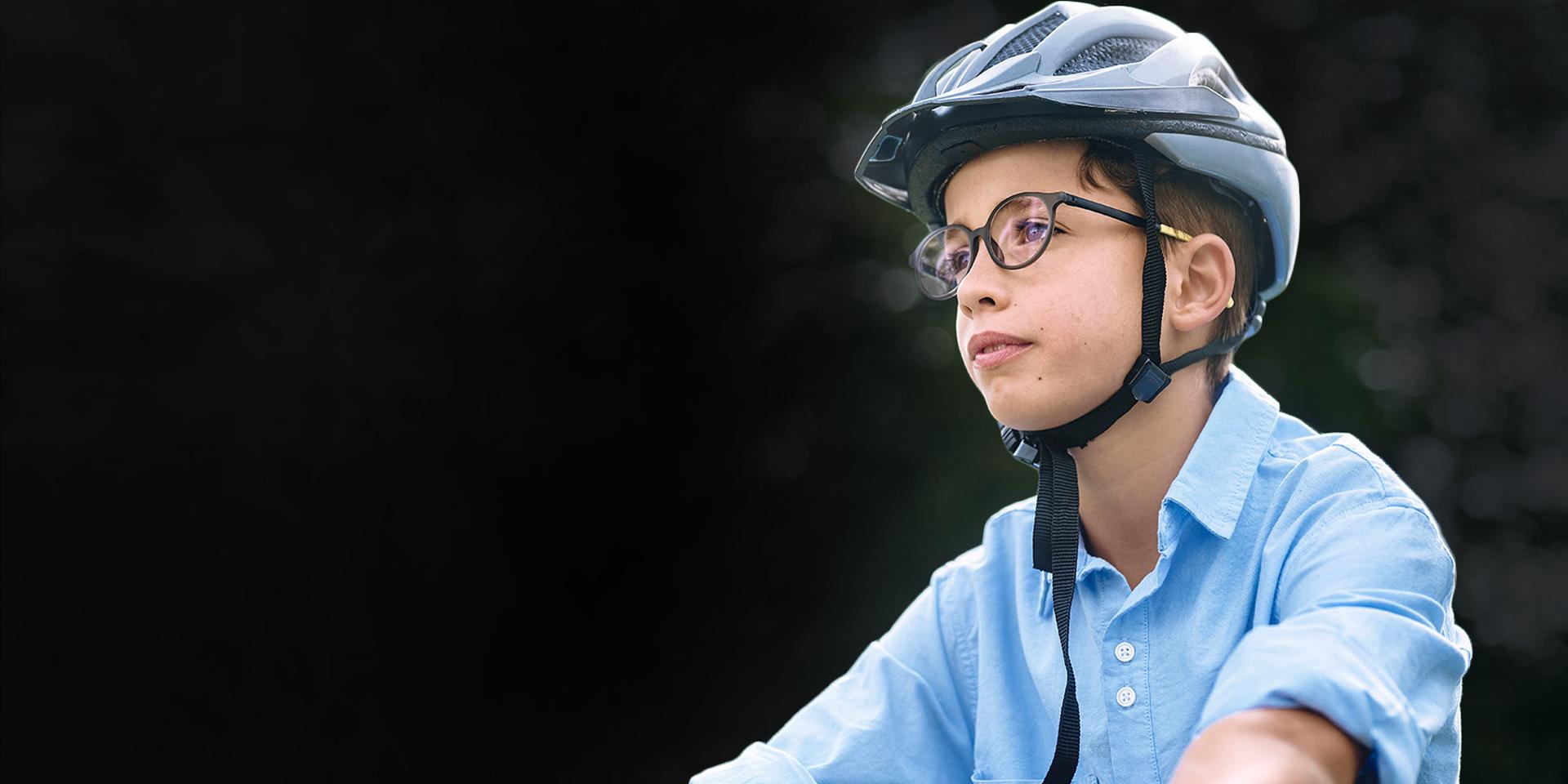 En dreng der kører på cykel i en park, og som bærer briller og cykelhjelm.
