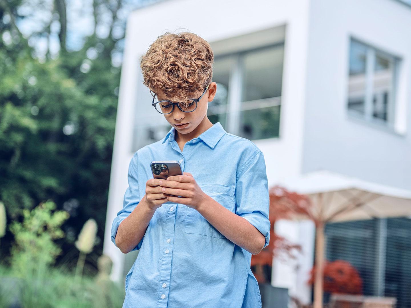 Lille dreng udenfor der ser på sin telefon.