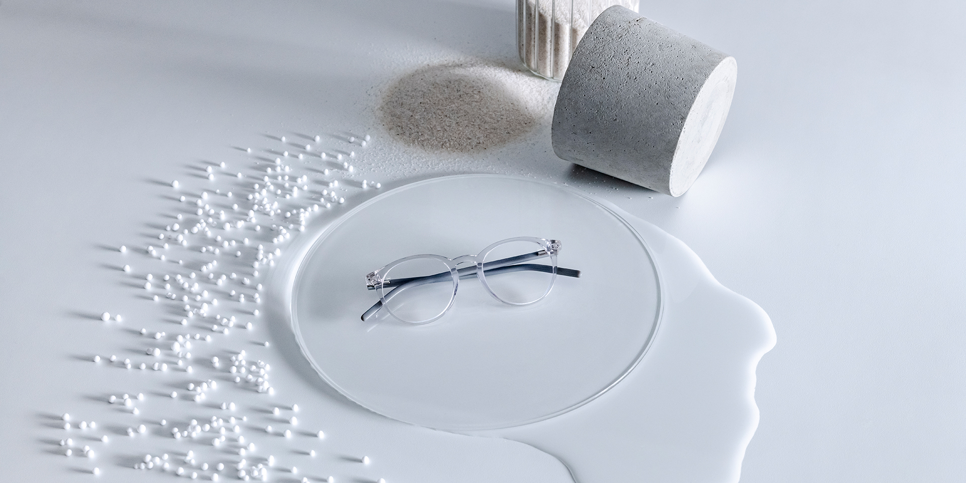 ZEISS brilleglas med DuraVision® coating anbragt på en glassokkel, omgivet af vand, sand, kugler og sten.