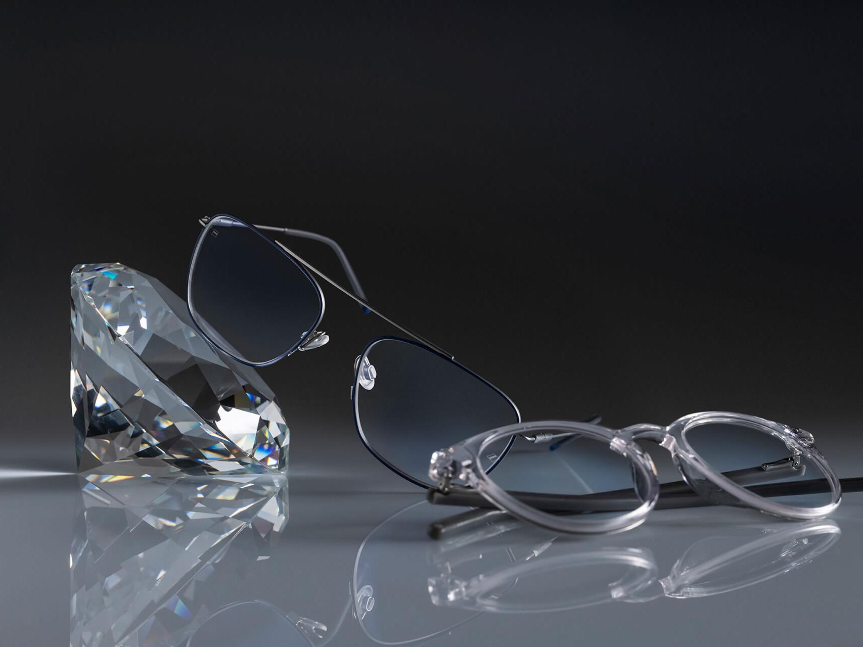 To par briller med ZEISS brilleglas, der har den hårdest ZEISS-coating nogensinde - DuraVision® Platinum. Et par briller ligger op ad et krystal, det andet ligger fladt ned på jorden. De udviser begge klare glas uden nogen blålig refleks.