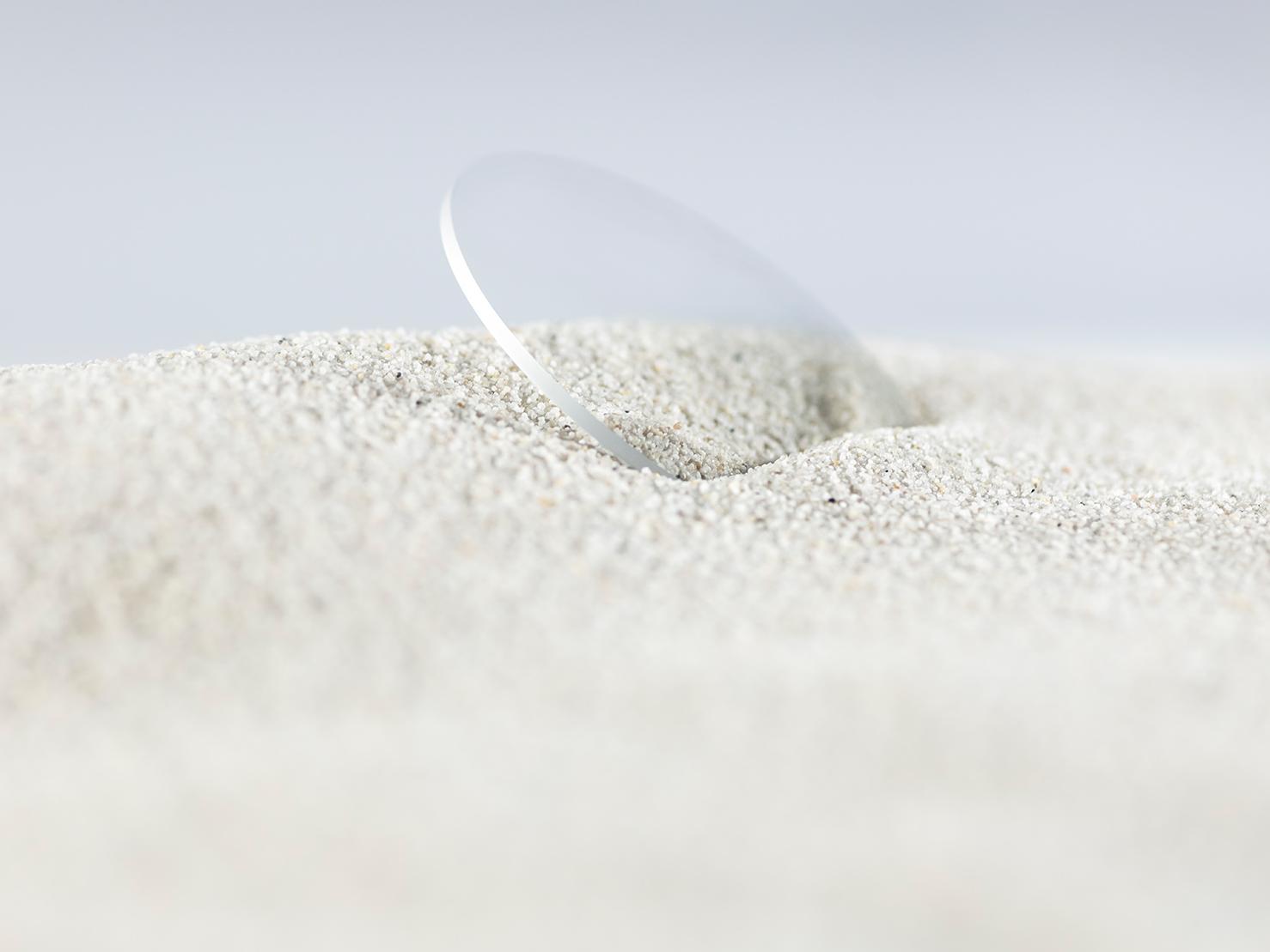 Et ZEISS brilleglas med en holdbar coating er dækket til med groft sand, men er stadig fri for ridser.