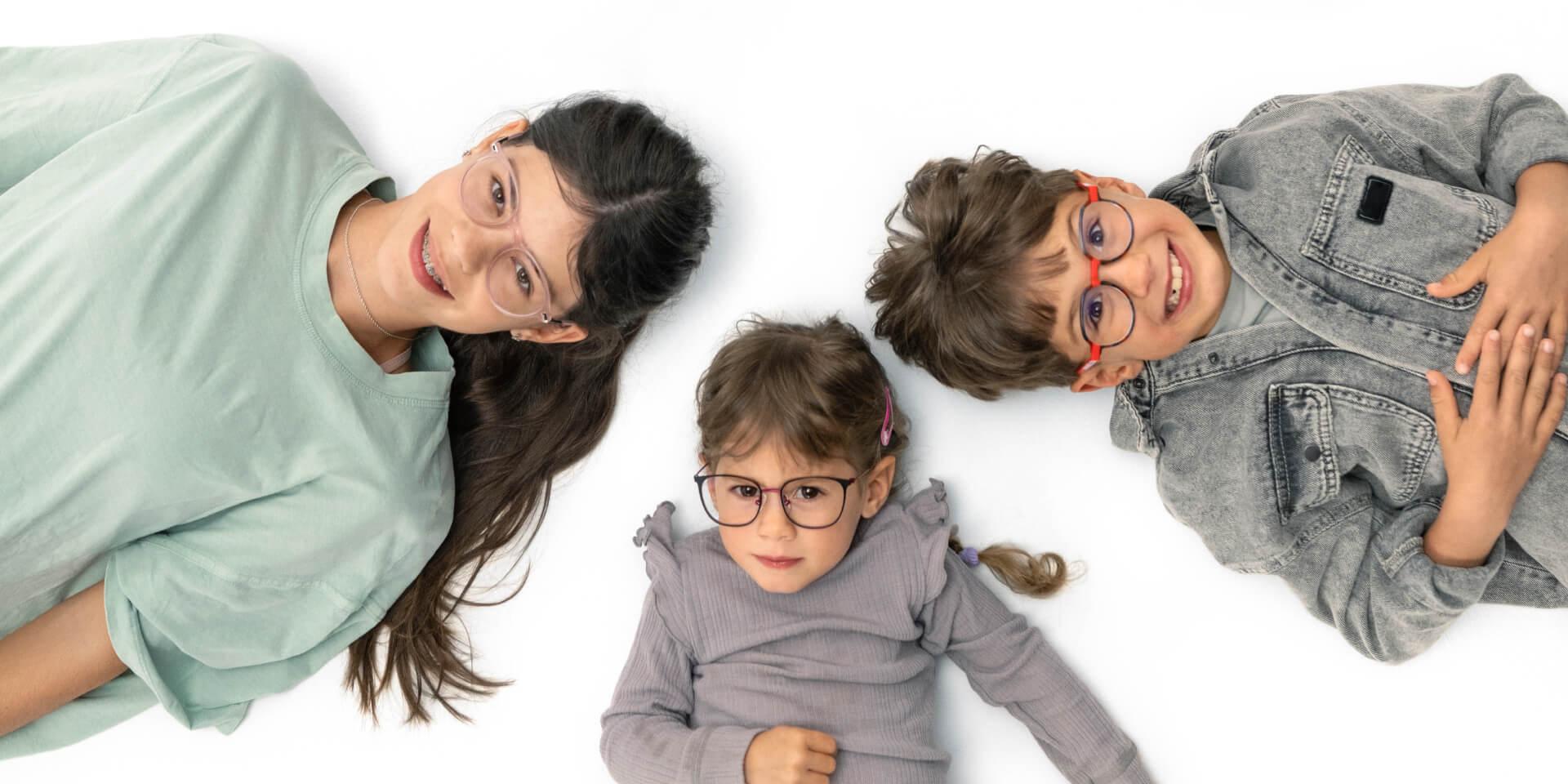 En teenager og to mindre børn ligger på gulvet og har ZEISS myopi-briller på.