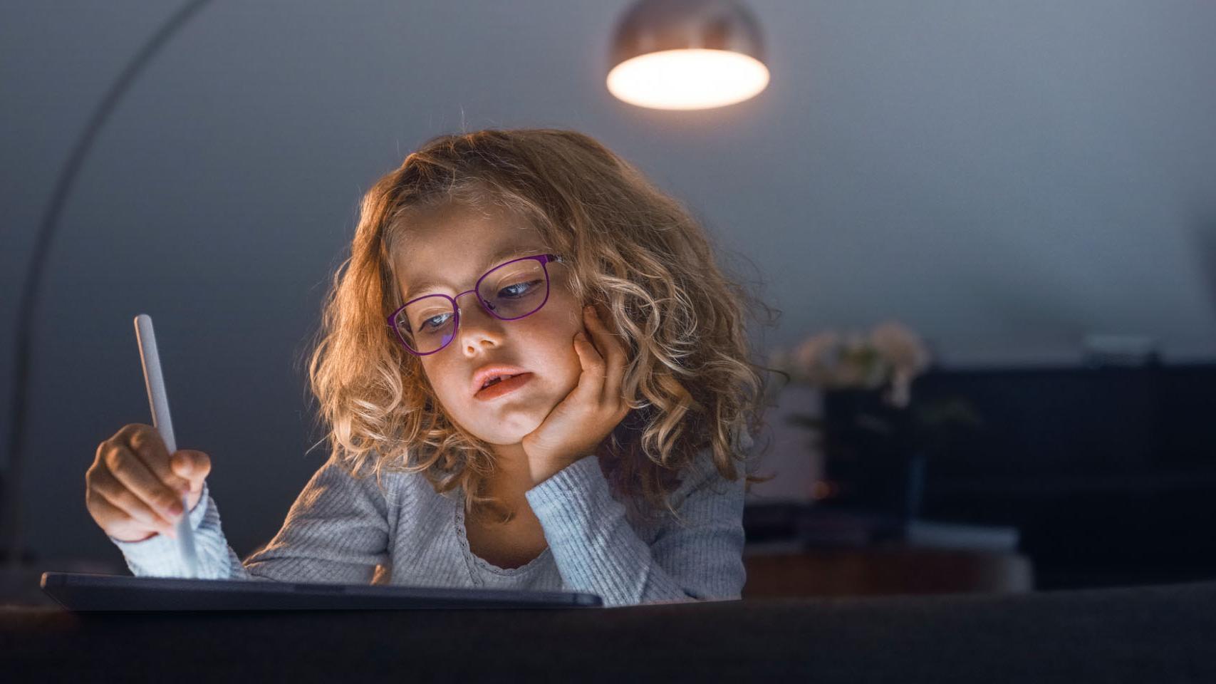 Lille pige i en mørk dagligstue kigger på en tablet.