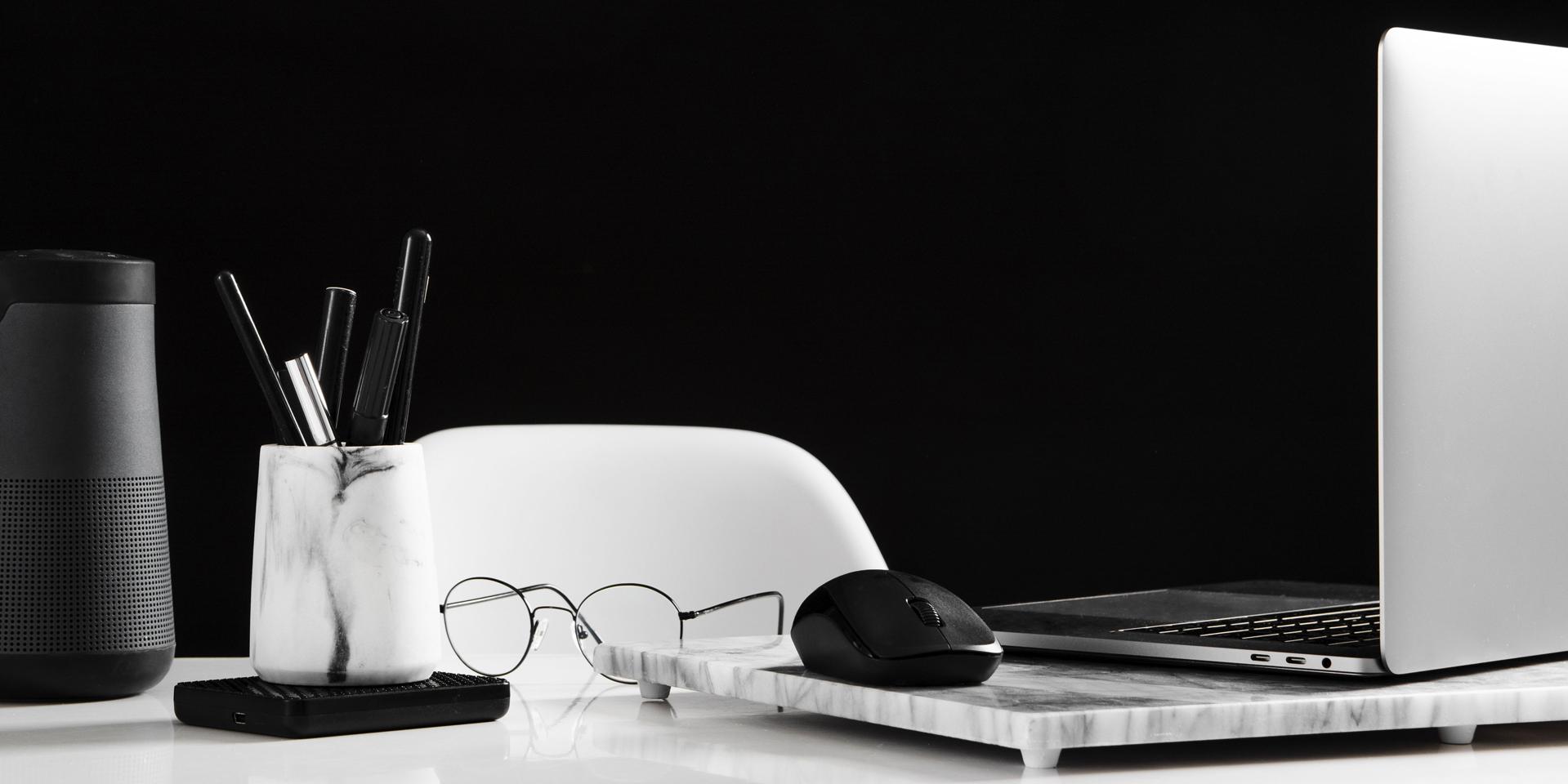 Ryddelig arbejdplads med en åben bærbar til højre og med en mus. Foran den ligger der et par briller. Til venstre i billedet er der en æske med penne.