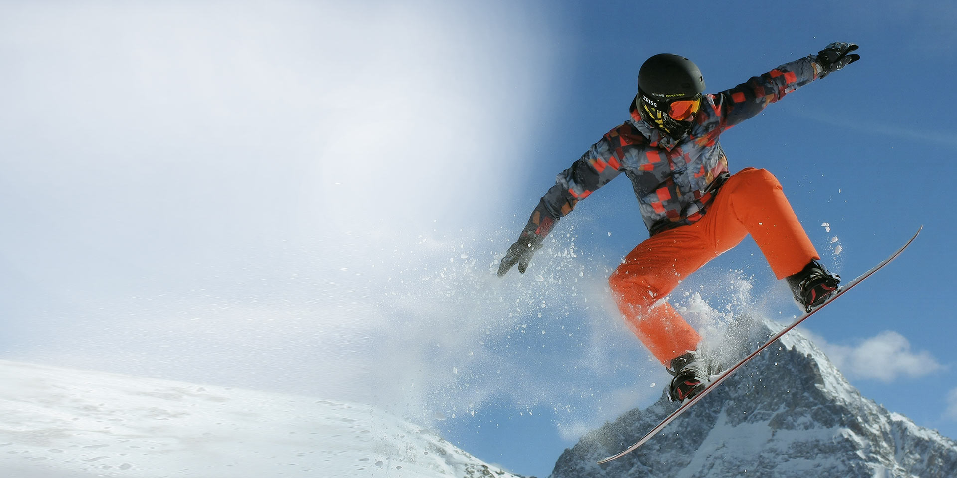 En mand springer med et snowboard, har en sort hjelm på og skibriller fra ZEISS med udskiftelig teknologi, der beskytter