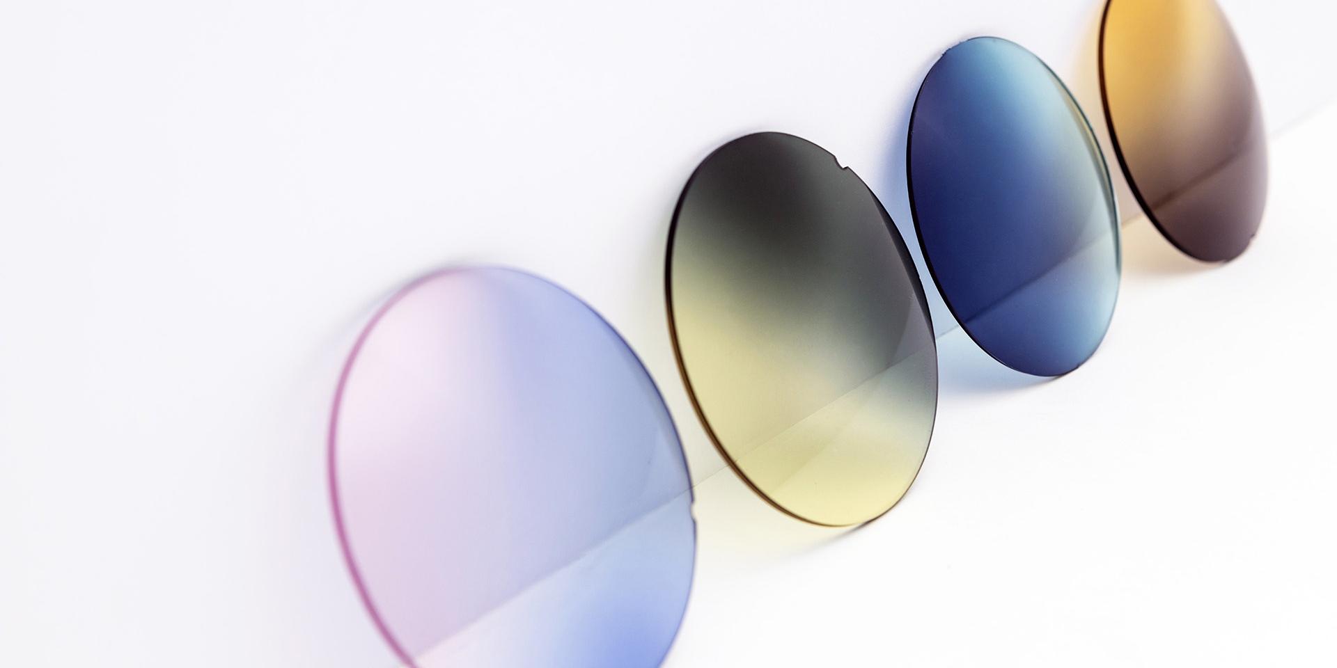 Forskelligt farvede solbriller der læner sig op ad en hvid overflade: pink-violette, gule-grå, blå og brune overgange.
