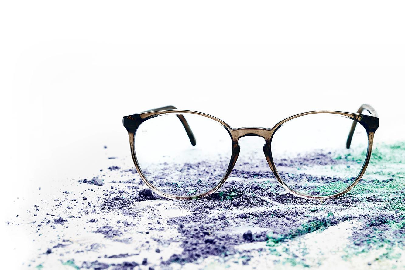 Et par briller med klare glas ligger på farverigt pulver.