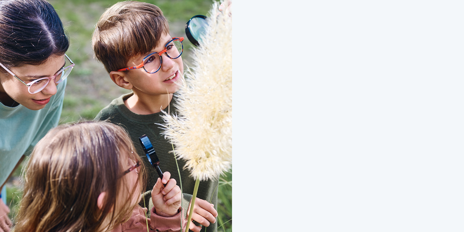 2 piger og 1 dreng med ZEISS MyoCare-brilleglas. De kigger på en plante, og to af de tre børn kigger på planten gennem et forstørrelsesglas.