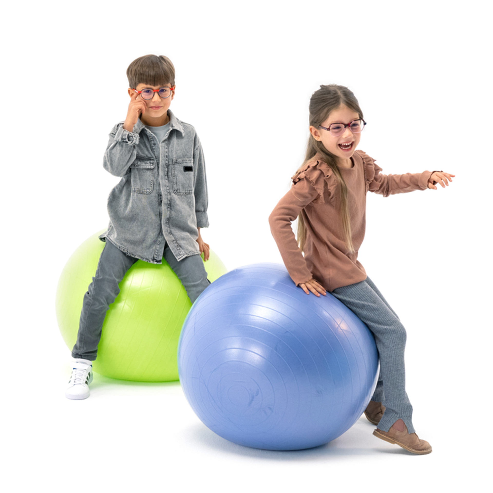 En dreng og en pige, der begge bærer briller, morer sig med at hoppe på hoppebolde.
