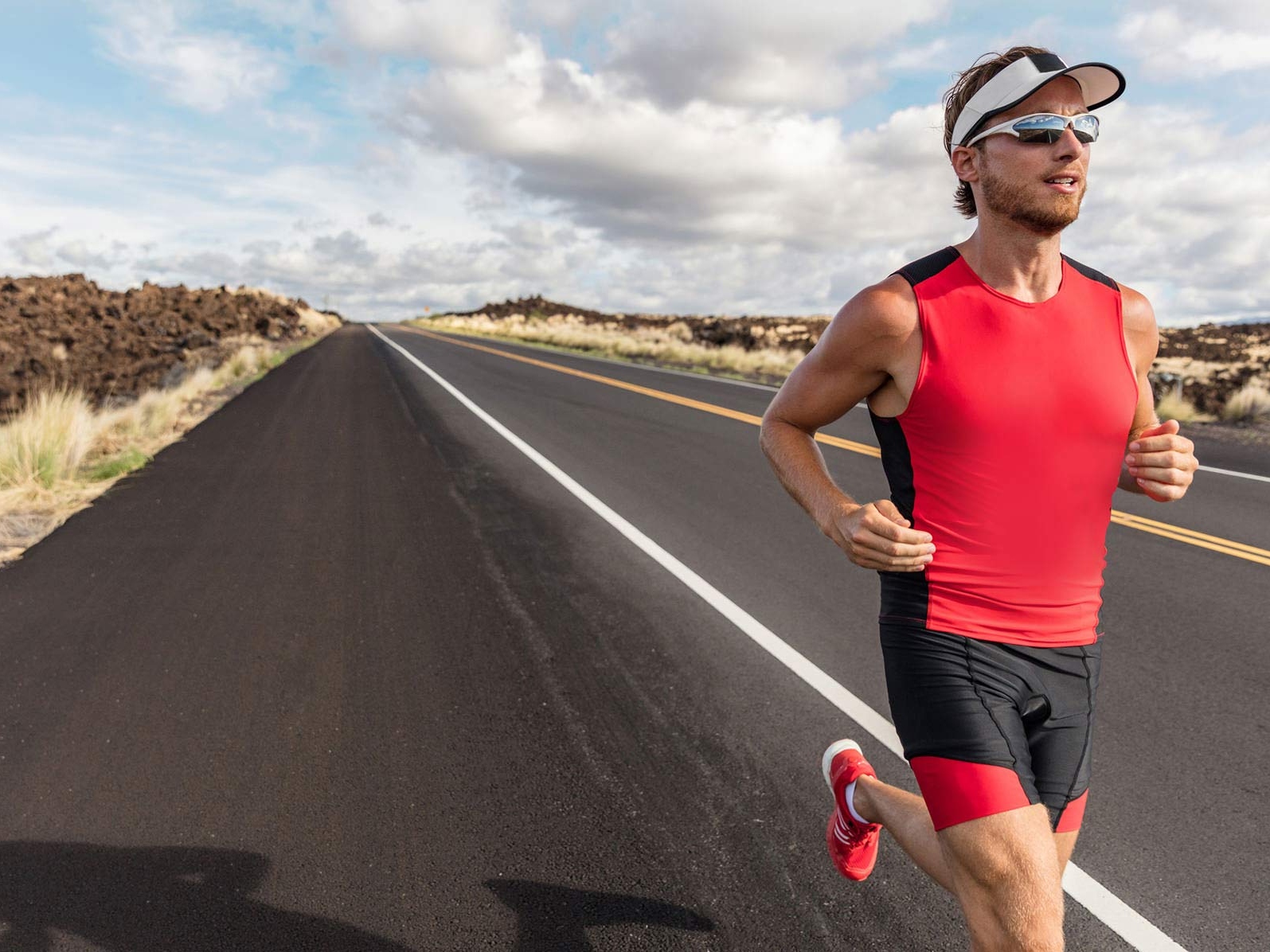 Et billede af en mand der har sportstøj og som bærer sportsbriller, mens han løber ned ad en vej. 