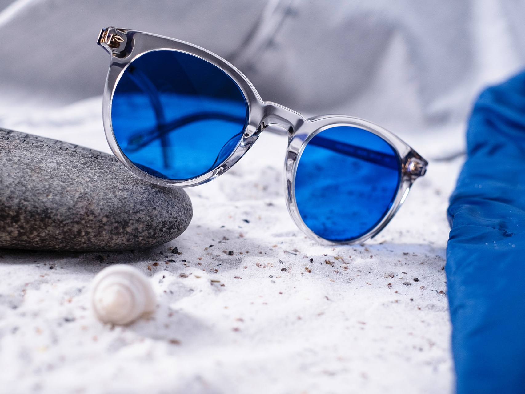 Billede af et par solbriller med blå farve lagt halvt ind over en sten