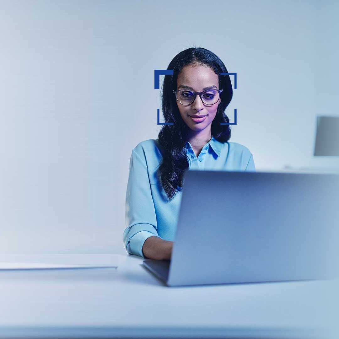 Sorthåret kvinde med briller, som smilende ser på en laptop