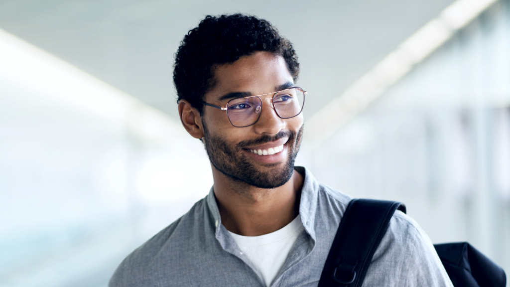 En ung mand der smiler, med en rygsæk over skulderen bærer ZEISS Digital SmartLife briller og ser til siden.