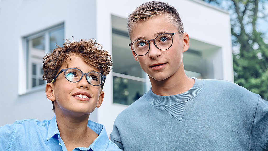En lille dreng ser op på en teenagerdreng; begge har ZEISS Single Vision SmartLife Young briller på